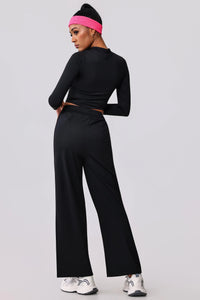 Woman in black long-sleeve crop top and wide-leg activewear pants with pink headband, styled for gym or casual wear.