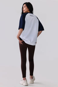 Woman in white and navy raglan activewear tee with 'SeanClaire' logo, paired with dark leggings and white sneakers