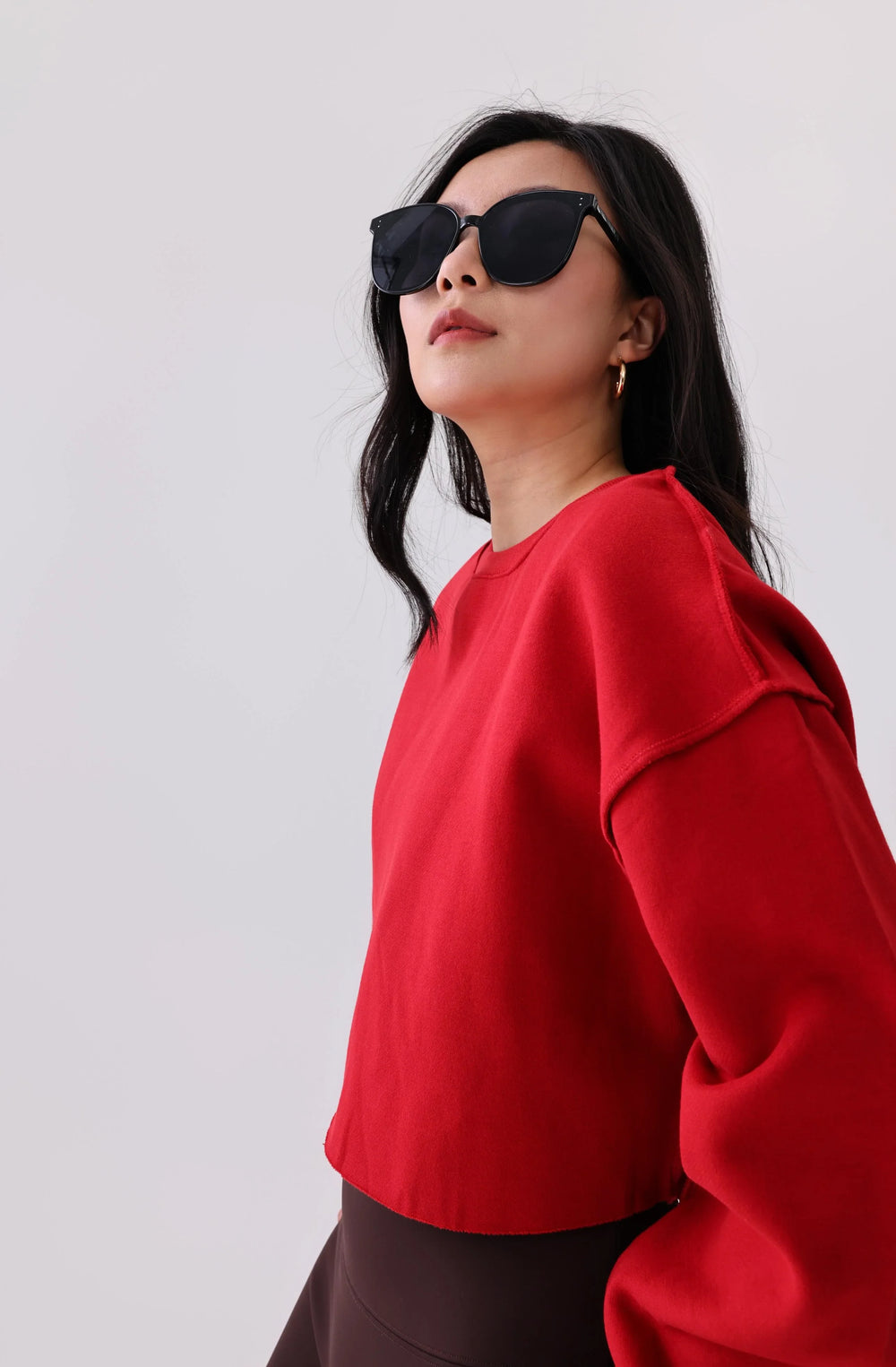 Woman in red activewear top and black leggings, wearing sunglasses, styled for fitness or casual wear.