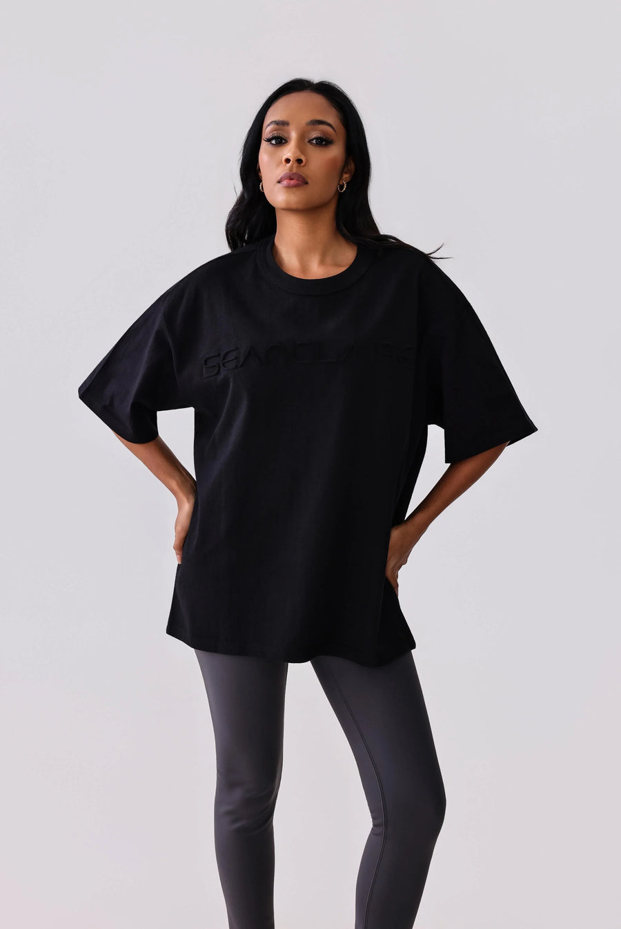 Woman wearing black oversized activewear tee with subtle logo, paired with grey leggings for workout or casual wear