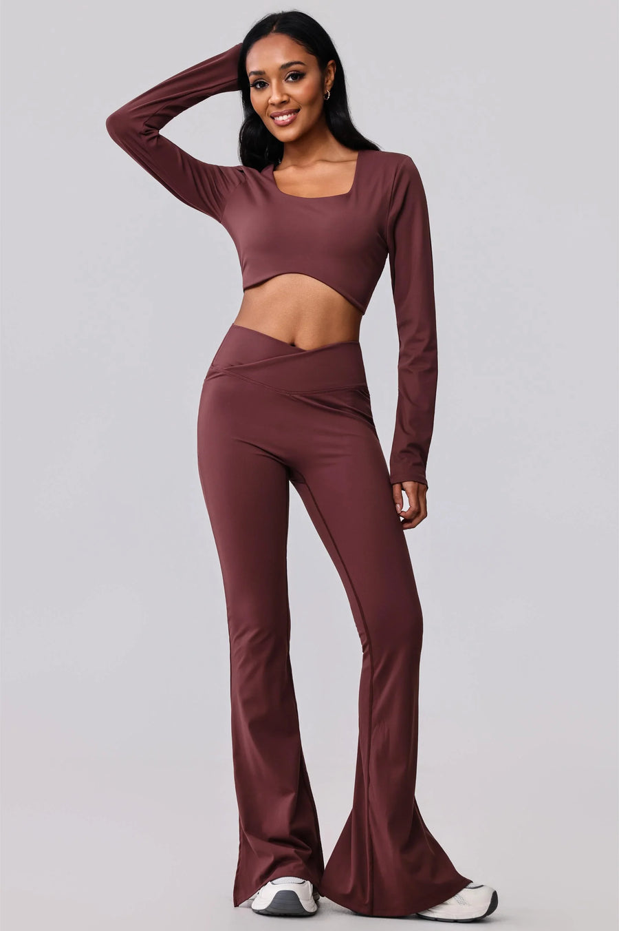 Woman in burgundy long-sleeve crop top and flared leggings, activewear set for yoga or gym