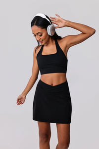 Woman in black sports bra and matching skirt with headphones, ready for workout or yoga