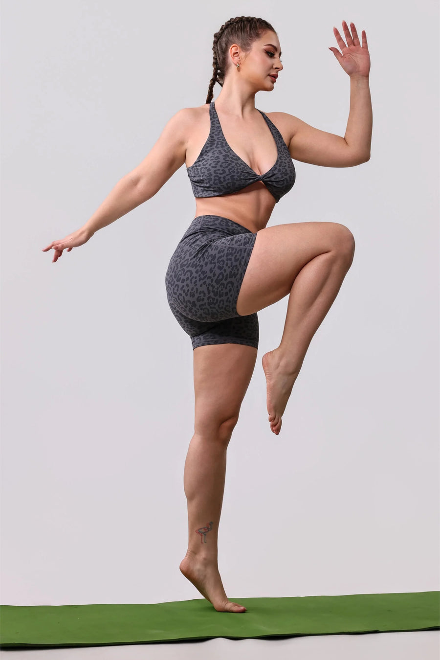 Woman in gray leopard print sports bra and shorts doing yoga pose on green mat