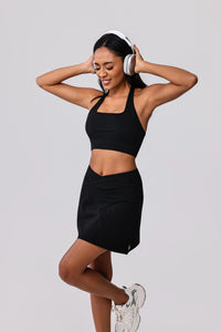 Woman in black sports bra and matching skirt with headphones, ready for workout or gym session