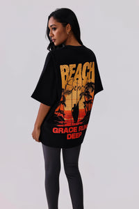 Black graphic tee with beach sunset print, palm trees, surfer silhouette, and 'Grace Runs Deep' text, paired with leggings.