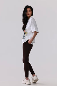 Woman in white floral tee and dark brown leggings with white sneakers, side view