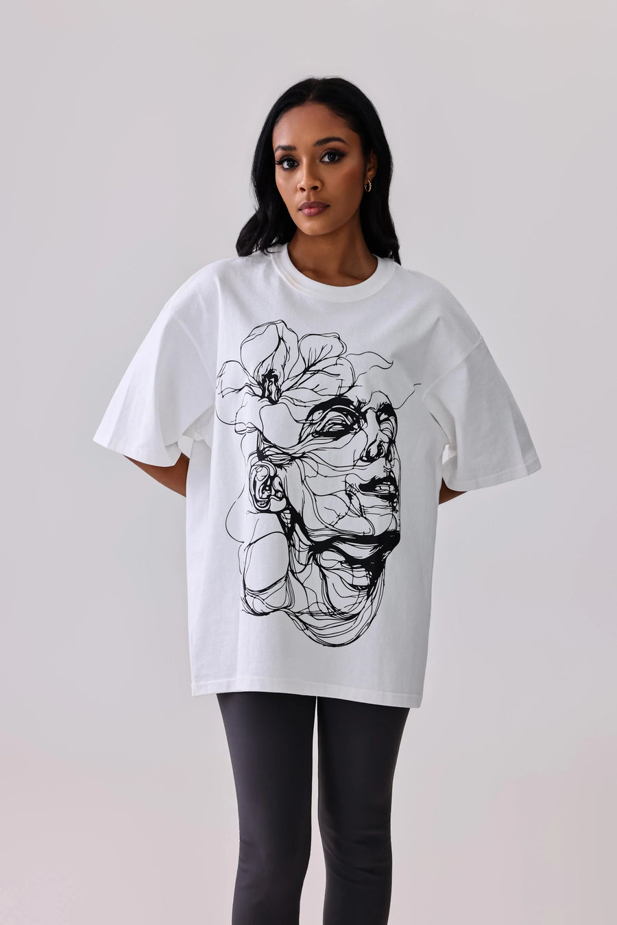 White oversized graphic tee with black floral and face line art, paired with black leggings for activewear