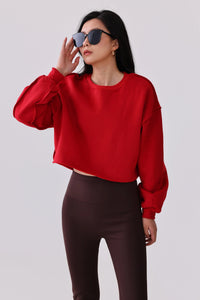 Woman in red cropped sweatshirt and brown leggings, wearing sunglasses, stylish activewear outfit