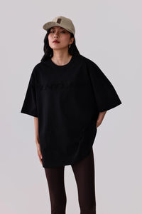Woman in black oversized t-shirt with subtle logo, paired with leggings and a beige cap for activewear style
