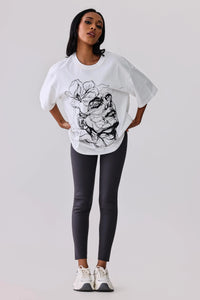 White graphic tee with abstract face print, paired with dark leggings and white sneakers for activewear