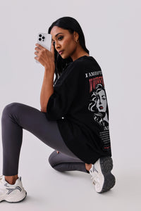 Woman in black graphic tee and gray leggings posing with phone, activewear outfit