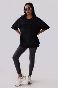 Woman in black oversized activewear tee, gray leggings, and white sneakers, styled with sunglasses for gym or streetwear.