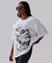 Woman in white oversized graphic tee with black floral print, styled with black leggings and sunglasses for activewear look
