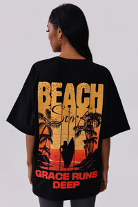 Black oversized graphic tee with beach surf sunset print, palm trees, surfer silhouette, and 'Grace Runs Deep' text