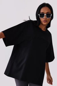 Woman in black oversized activewear tee with subtle logo, styled with white sunglasses for gym or casual wear